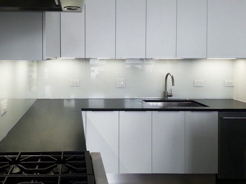 Kitchen corner with shiny white glass backsplash and black countertops for high contrast and modern look