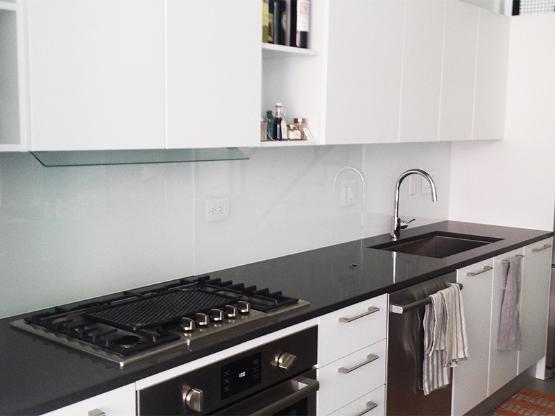 white kitchen cabinets and all white glass backsplash above black kitchen countertops