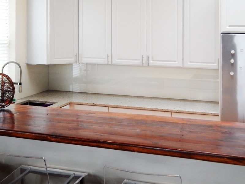 white kitchen cabinets and white kitchen countertops with mahogany breakfast bar and shiny white glass backsplash
