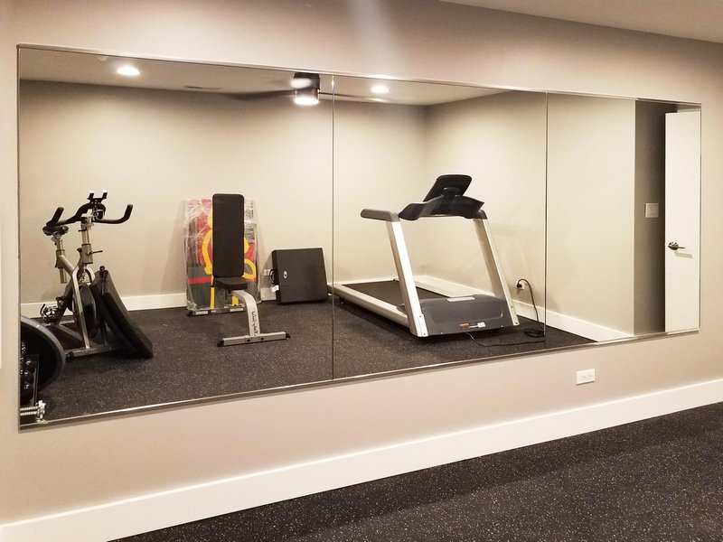 a long custom home gym mirror reflecting a weight bench, exercise bicycle, and treadmill