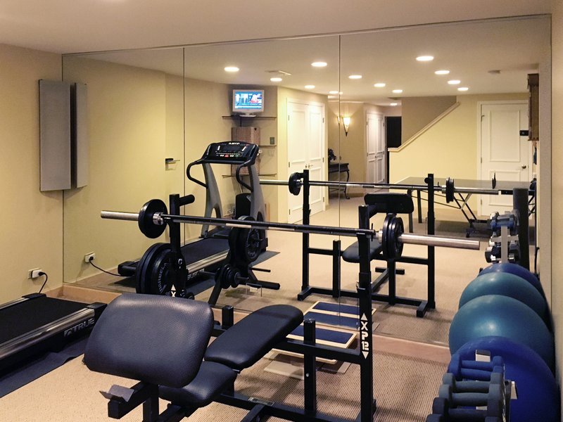 3 floor-to-ceiling mirror panels reflecting a treadmill and weight bench in a home gym