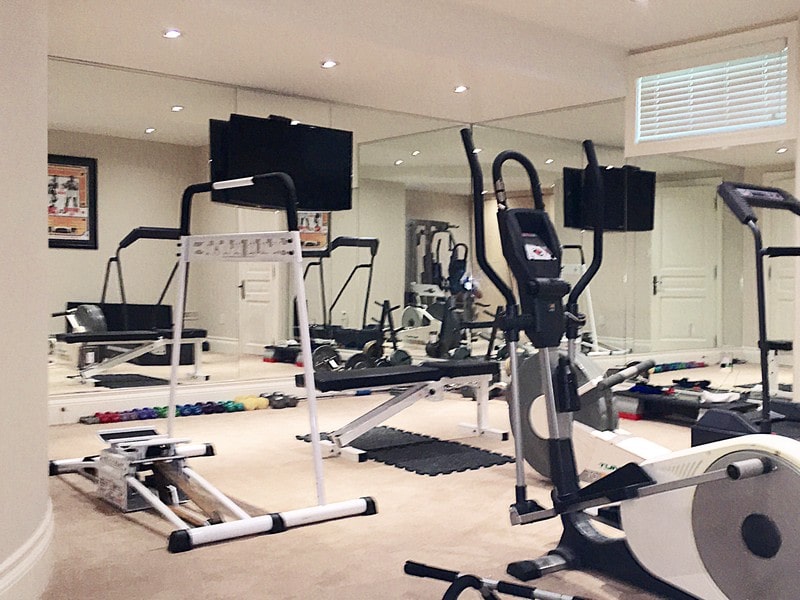 a home gym full of equipment like an exercise bike, free weights, and a weight bench in front of a wall that is covered top-to-bottom and side-to-side in custom mirrors