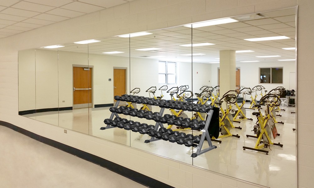 six mirror panels along a wall in a group exercise room full of free weigths and cardio equipment
