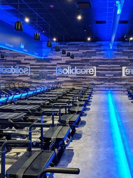 blue light shining on a group exercise room in a fitness center with large custom mirrors on one wall and a solidcore logo over brick on the other wall