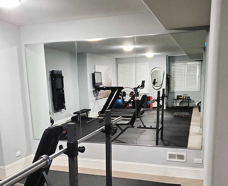 four large frameless mirrors filling the back wall of a home gym set up inside a garage