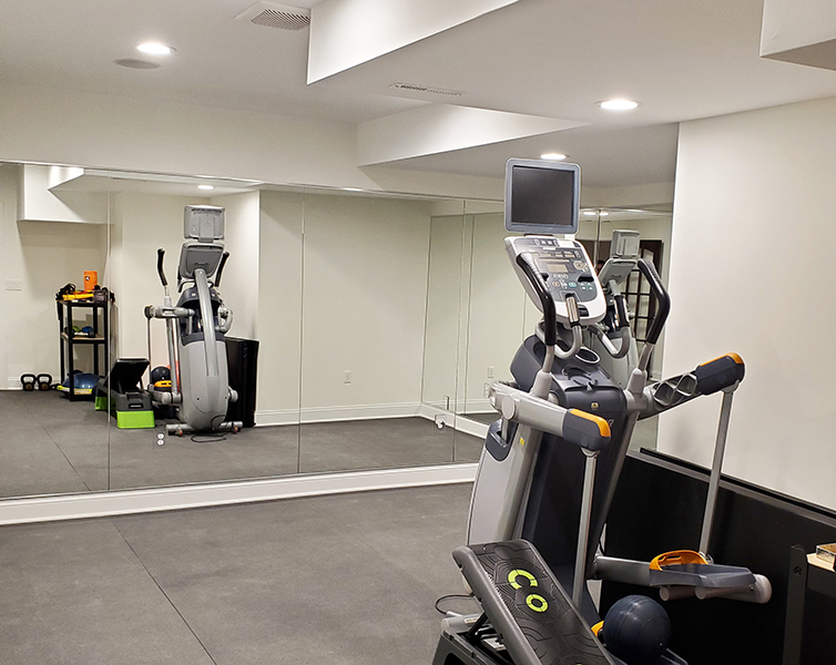 3 floor-to-ceiling mirror panels reflecting a treadmill and weight bench in a home gym
