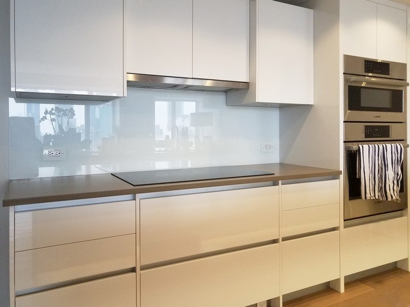 all white kitchen with built-in stainless steel double oven and a shiny, seamless white glass backsplash