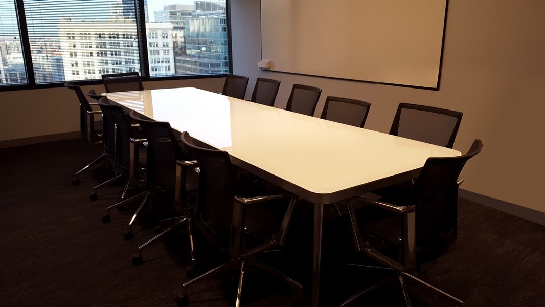 large conference table with white painted glass table top surrounded by modern office chairs on wheels